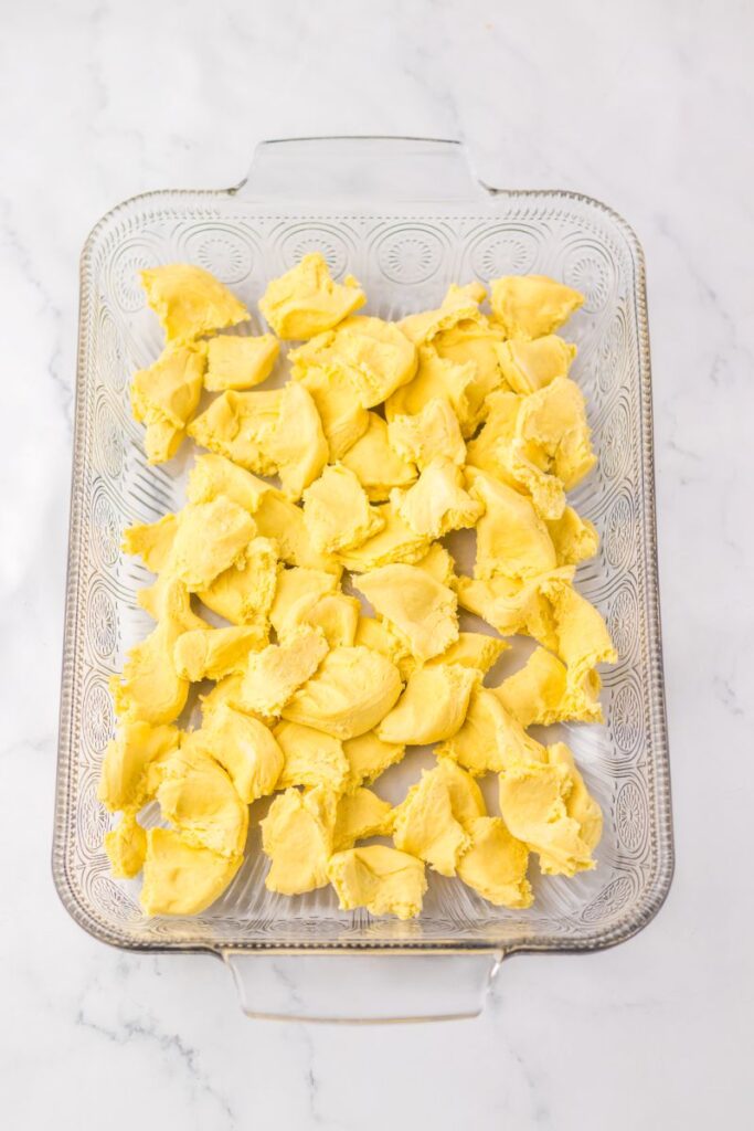 Overhead view of clear casserole dish with chopped up raw biscuit dough.