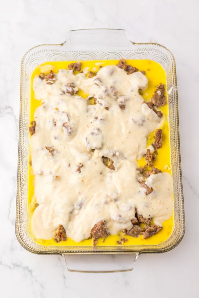 Overhead view of white gravy, sausage, and eggs in glass casserole dish.