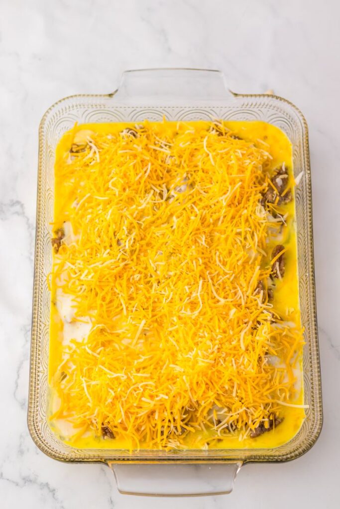 Overhead view of eggs, gravy, and sausage topped with shredded cheese in glass casserole dish.