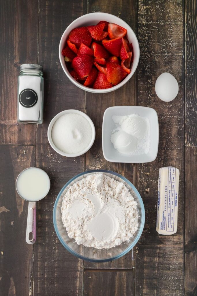 Ingredients for strawberry coffee cake in white bowls on wooden background.
