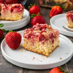 Close up of one piece of strawberry coffee cake on white plate next to whole strawberries.