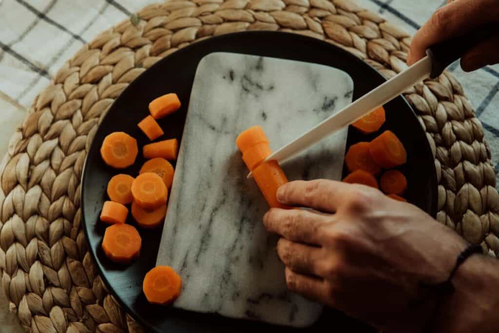 Hands chopping a carrot on a marble cutting board.
