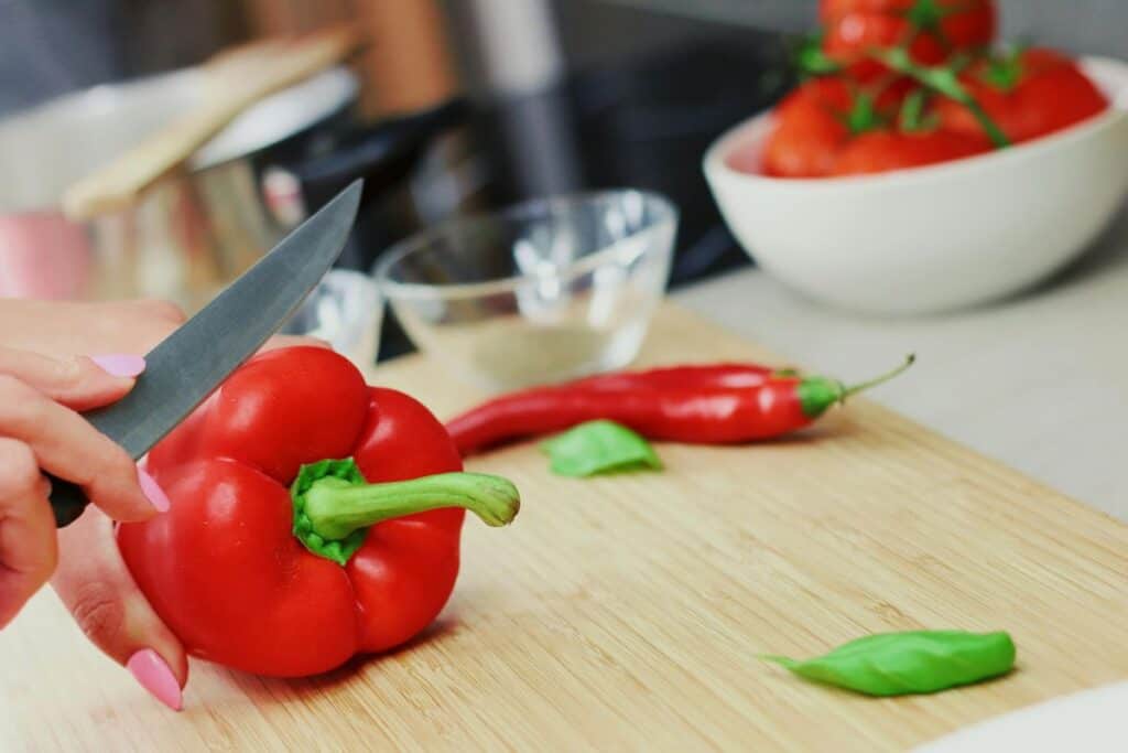 Hand chopping a red pepper on a wooden cutting board.