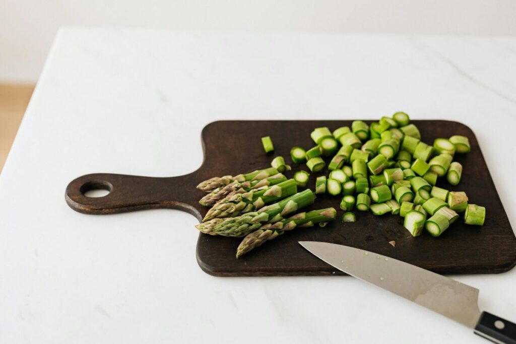 Cut up asparagus on wooden cutting board next to knife.