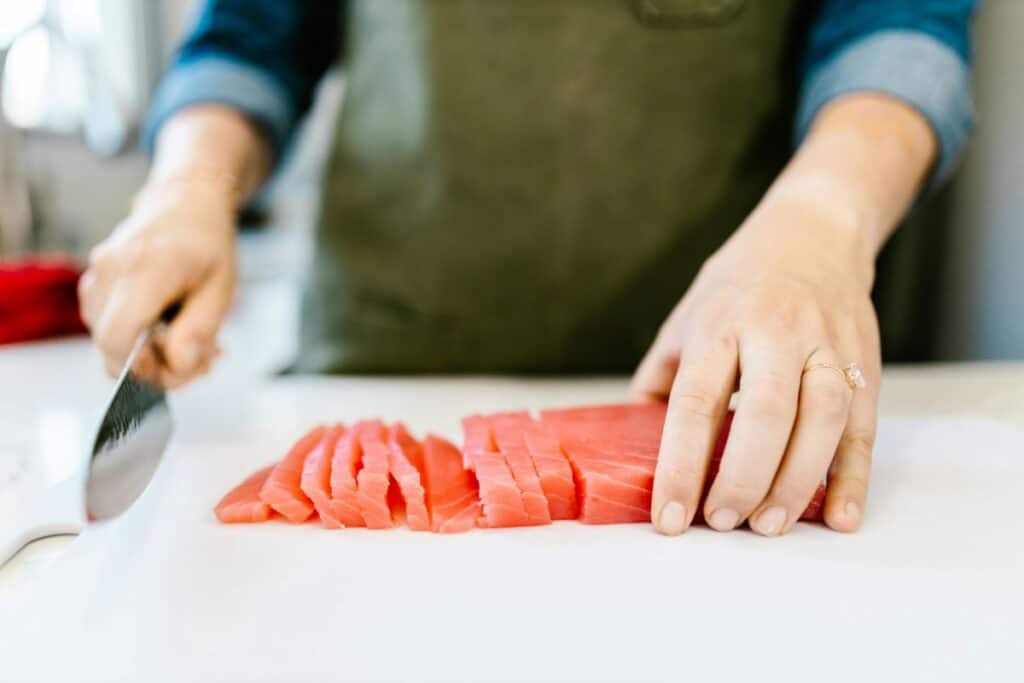 Hand chopping raw salmon on plastic cutting board.