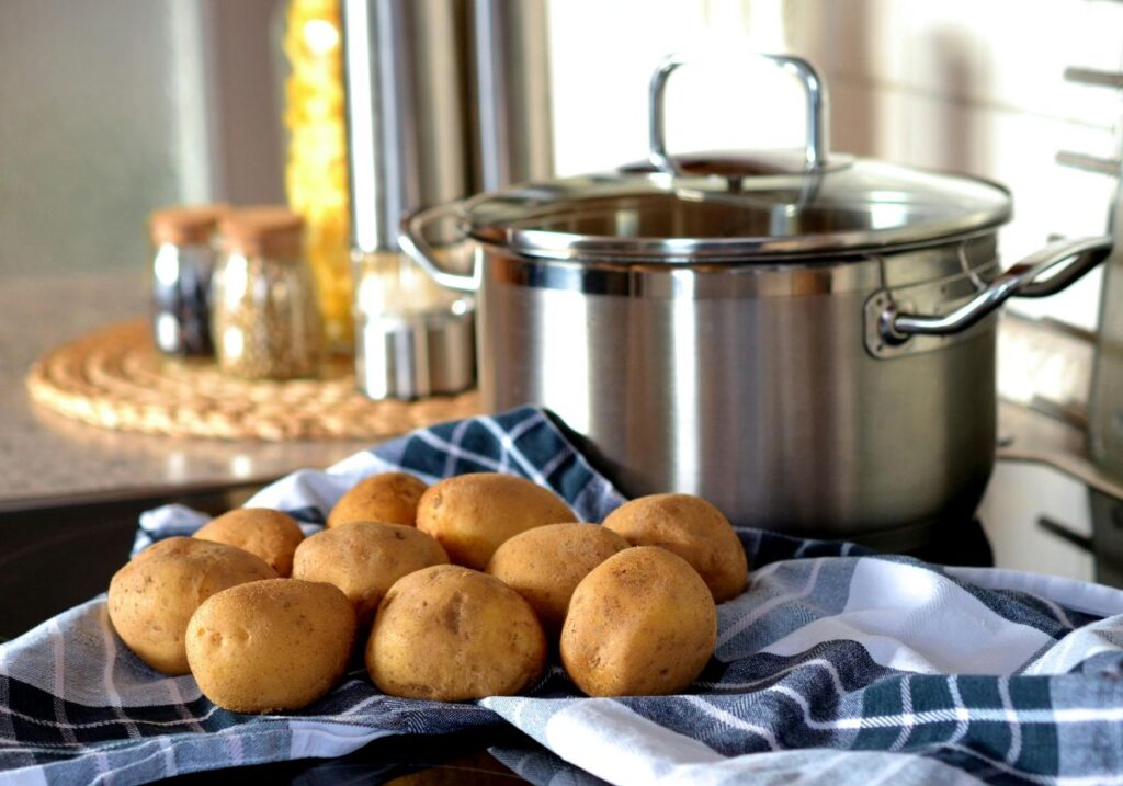 Side view of potatoes on blue cloth in front of silver pot.