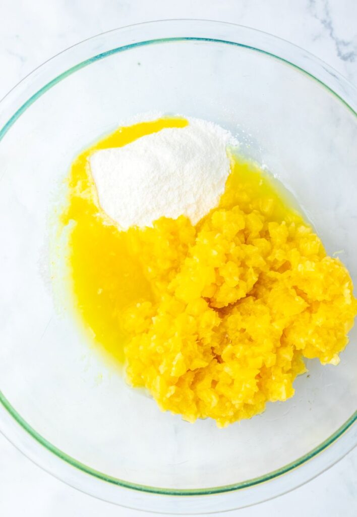 White powder in chopped pineapple and yellow juice in glass bowl.