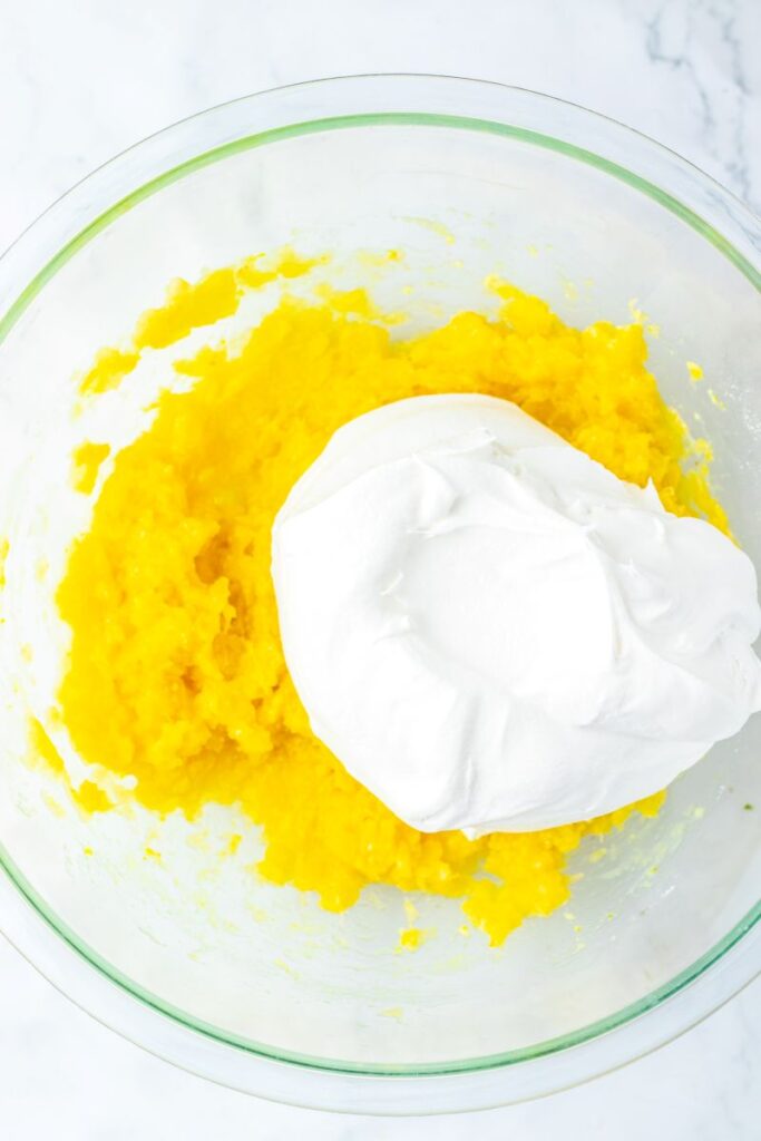 White cream on top of yellow chunky mixture in glass bowl.