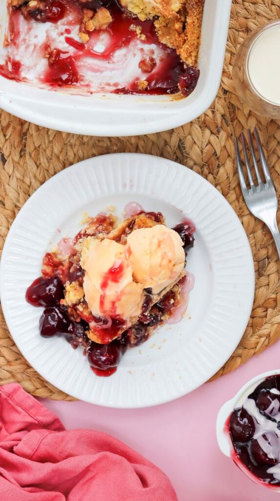 Overhead view of cherry dump cake topped with ice cream on white plate.