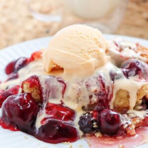 Close up of one serving of cherry dump cake topped with ice cream on white plate.