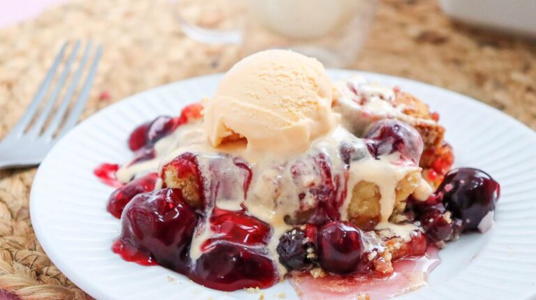 Close up of one serving of cherry dump cake topped with ice cream on white plate.