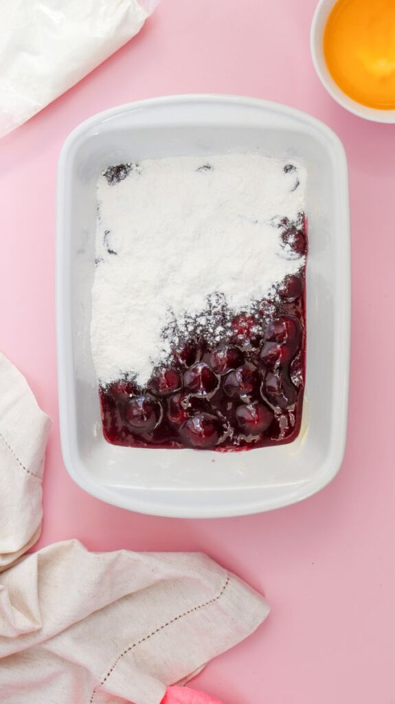 Overhead view of white rectangular baking dish with cherry pie filling topped with white powder.