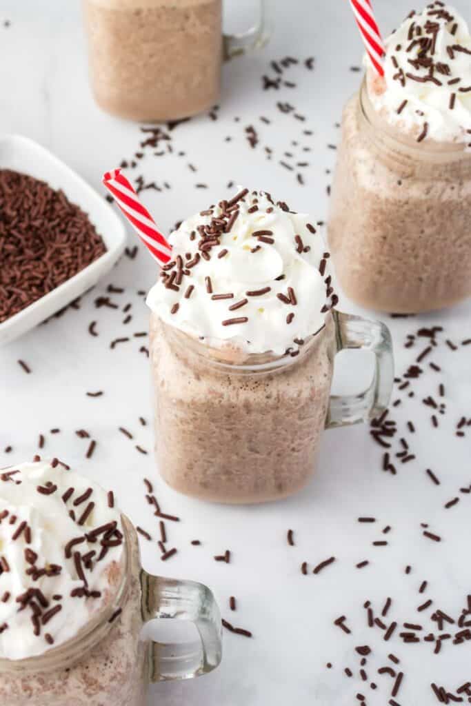 Overhead view of four chocolate milkshakes with whipped cream and chocolate sprinkles.