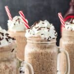 Side view of four chocolate milkshakes with whipped cream and chocolate sprinkles.