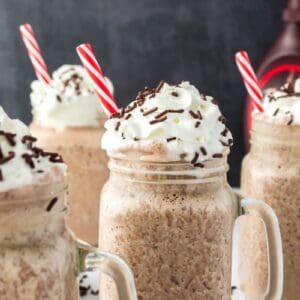 Side view of four chocolate milkshakes with whipped cream and chocolate sprinkles.