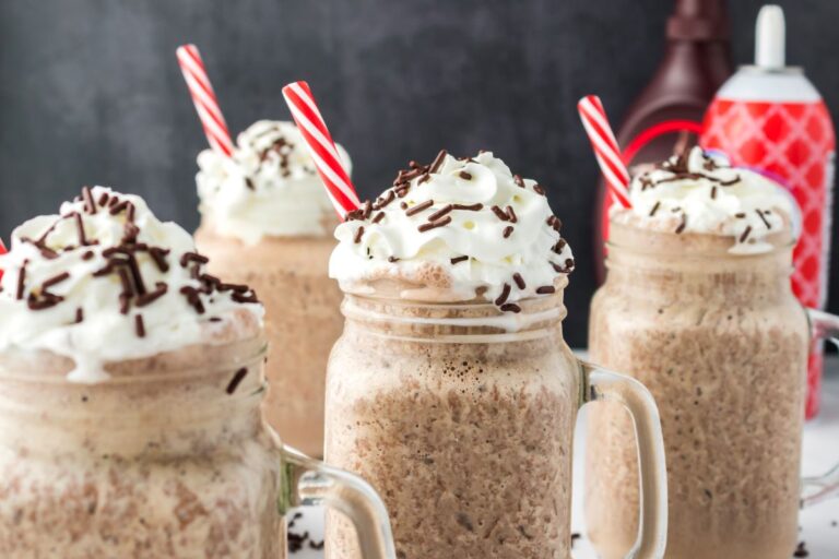 Side view of four chocolate milkshakes with whipped cream and chocolate sprinkles.