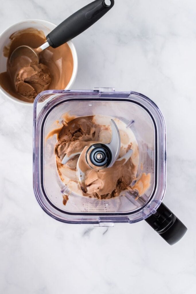Overhead view of blender with chocolate ice cream and milk inside.