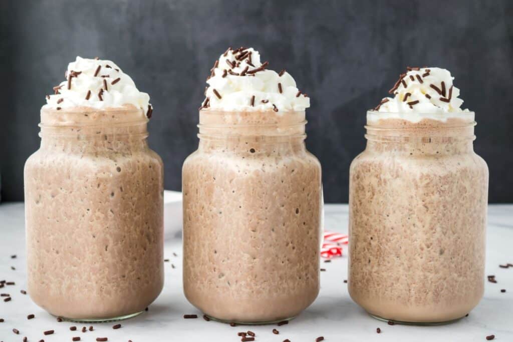 Side view of three chocolate milkshakes with whipped cream and chocolate sprinkles.