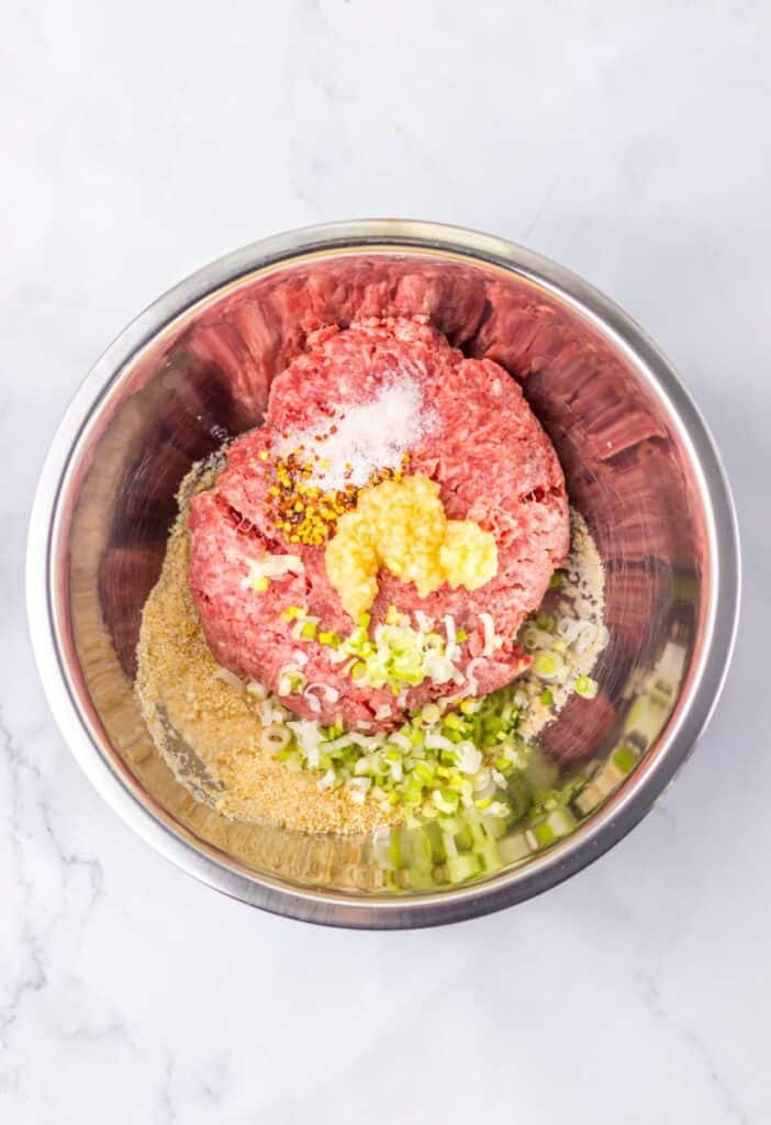 Silver bowl with ground beef, minced garlic, chopped scallions, and salt.