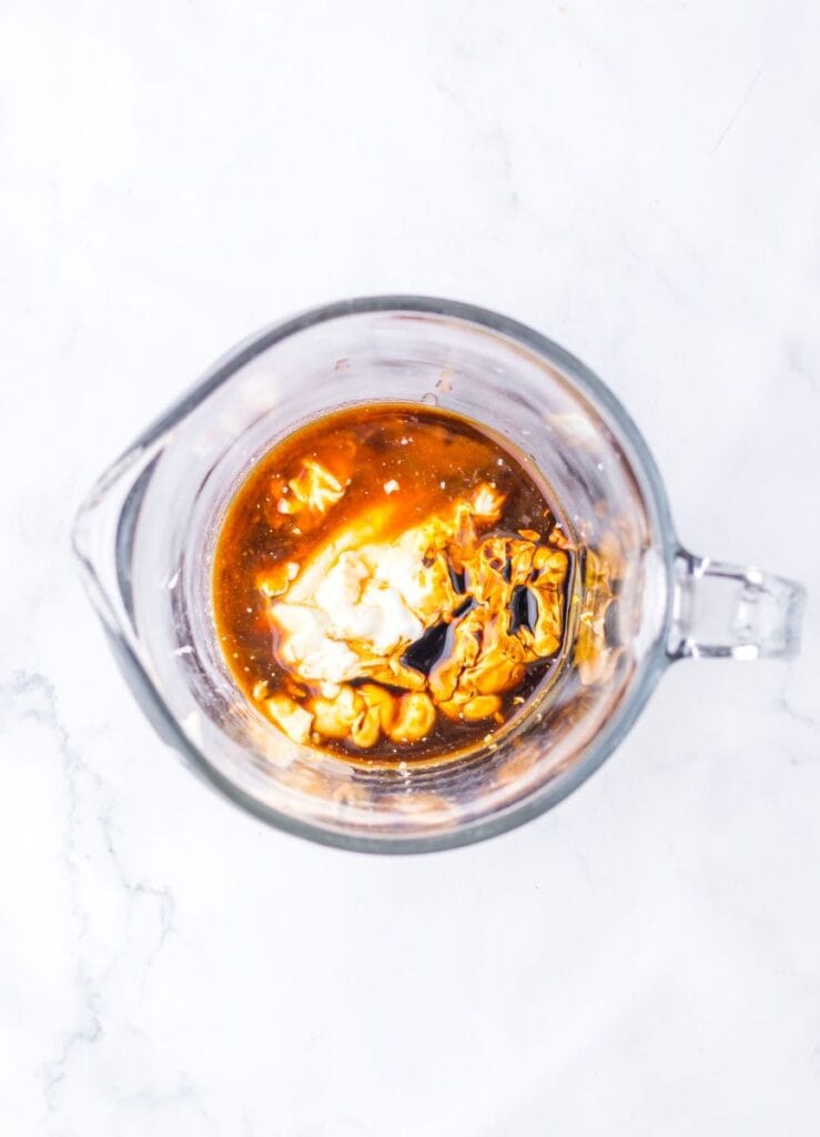 Clear glass measuring cup with dark brown liquid and mayonnaise and sour cream.