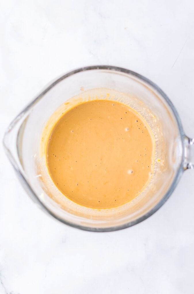 Overhead view of tan-colored sauce in glass measuring cup.