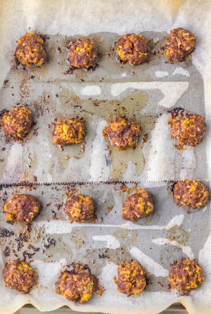 Overhead view of 16 cooked meatballs on parchment paper lined baking sheet.