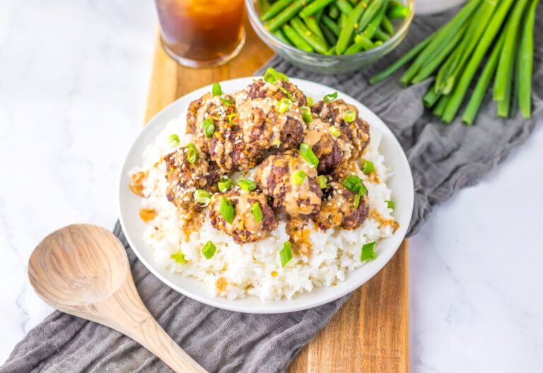 Meatballs over white rice on white plate with dark brown drink in the background.