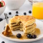 Side view of four griddle cakes with triangle shape missing and on fork on white plate topped with syrup.