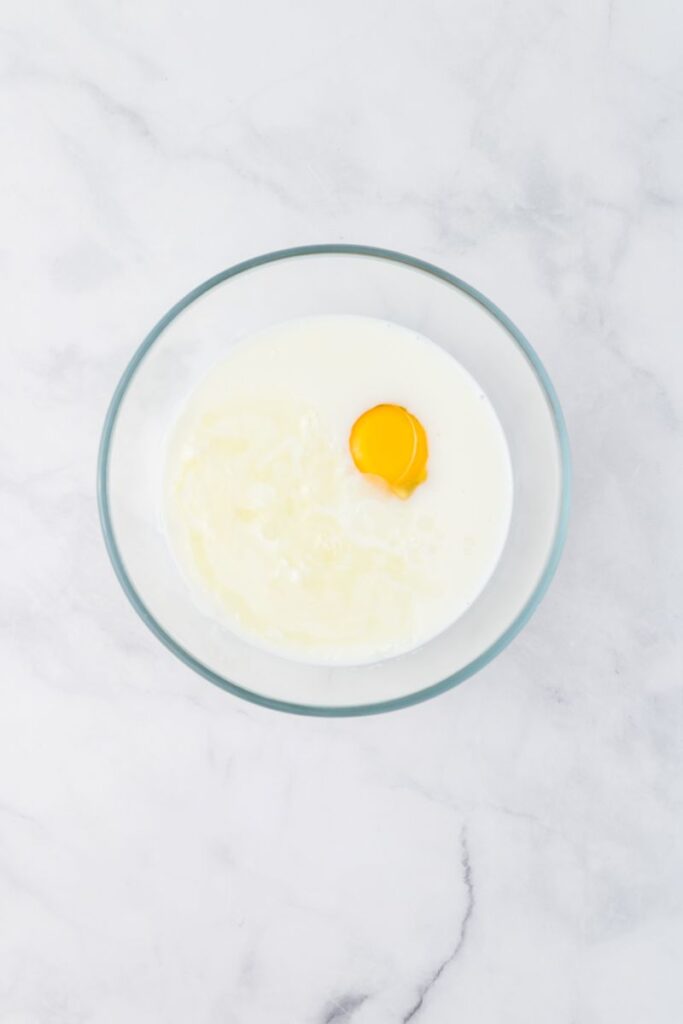 Overhead view of glass bowl with milk and an egg yolk on white background