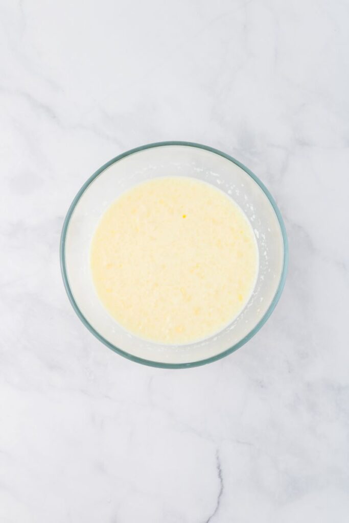Overhead view of creamy mixture in glass bowl on white surface.
