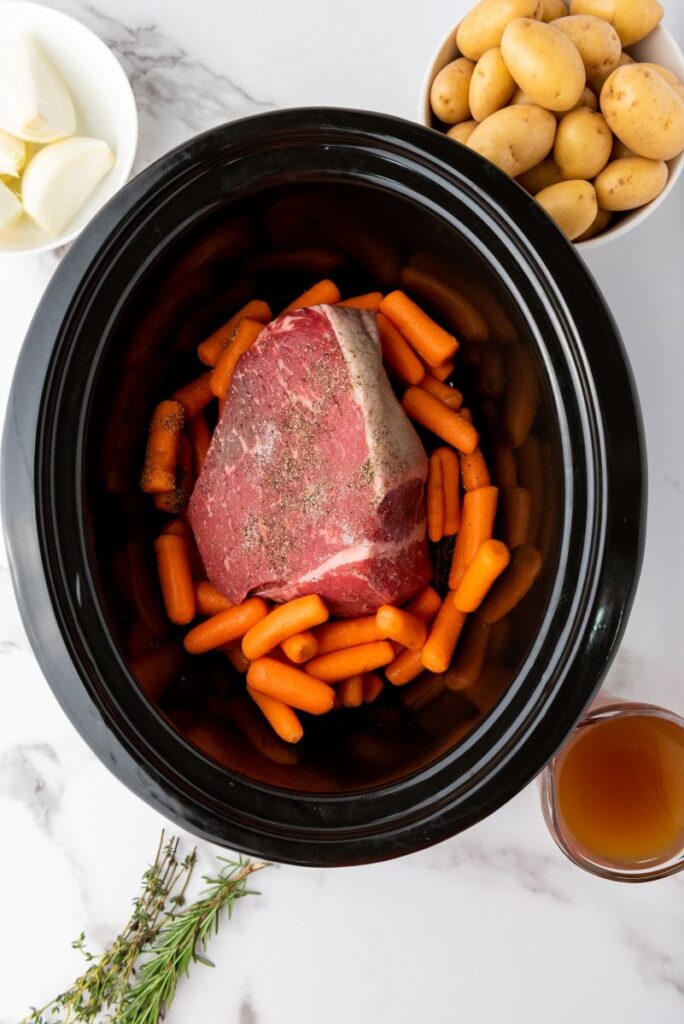 Overhead view of crockpot containing carrots and rump roast.