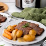 Three square cuts of beef with potatoes, onions, and baby carrots on white plate.