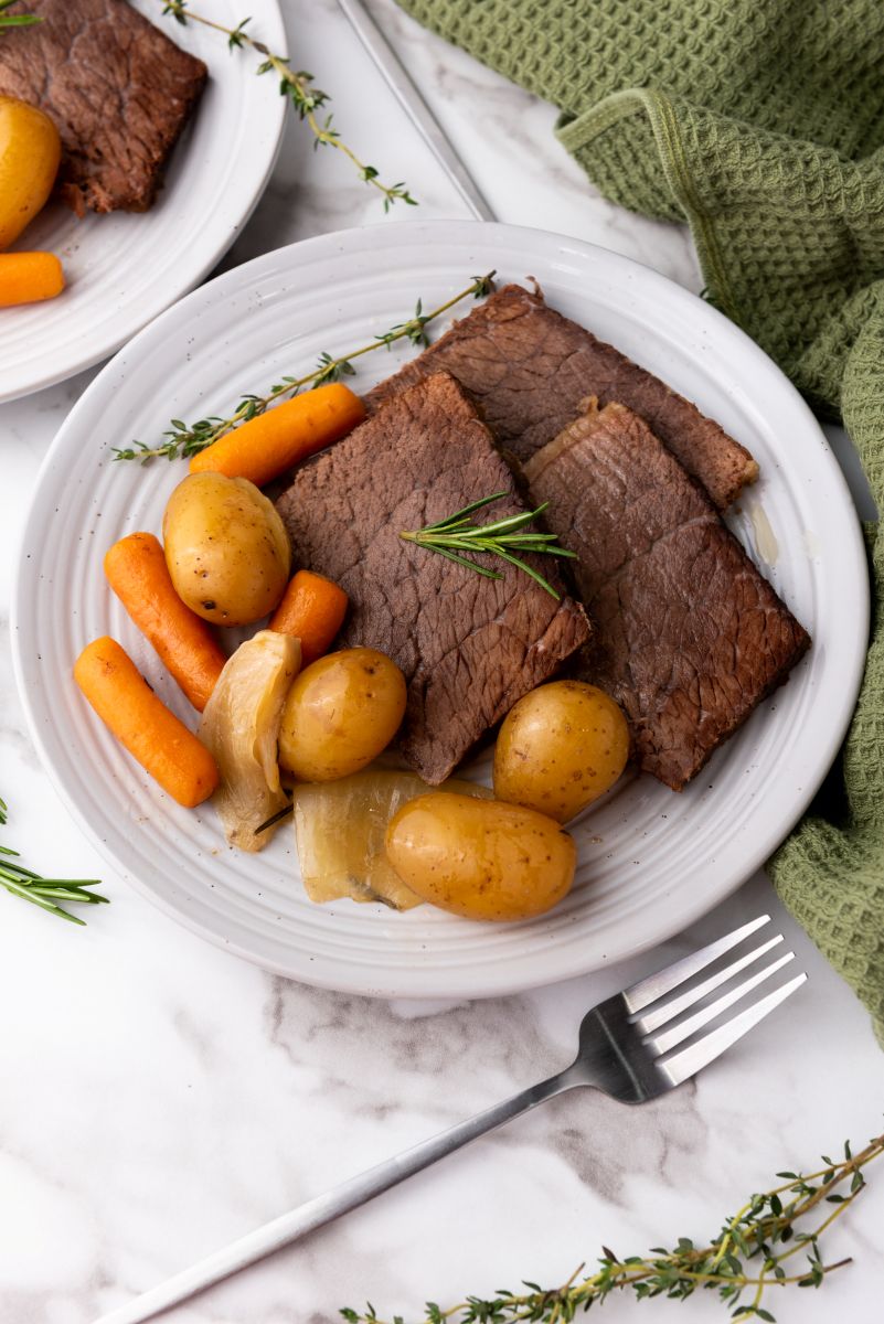 Three square cuts of beef with potatoes, onions, and baby carrots on white plate.