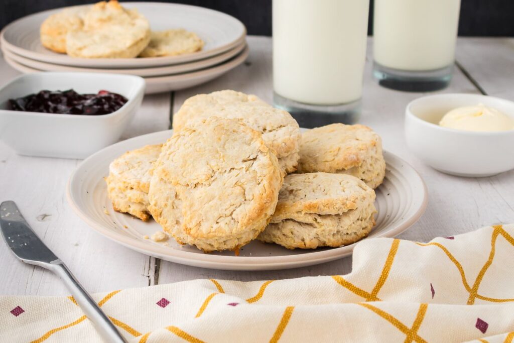 Side view of six biscuits on white plate with jam and butter in the background.