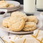 Side view of six biscuits on white plate with jam and butter in the background.