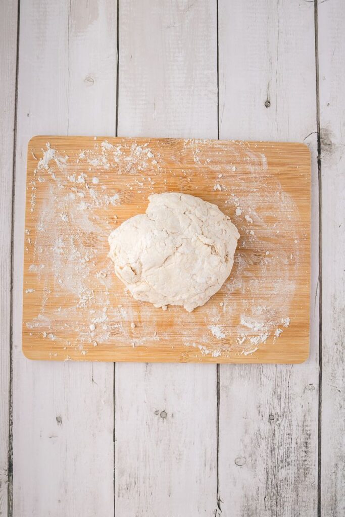 Overhead view of ball of bread dough on wooden cutting board.