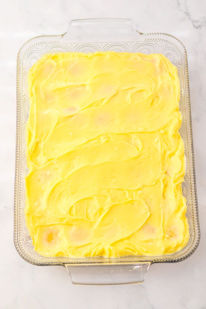 Yellow pudding spread on top of round cookies in rectangular glass dish.