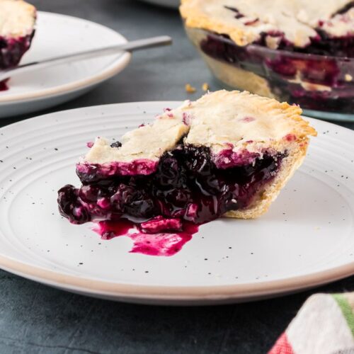 Side view of one slice of blueberry pie on white plate.