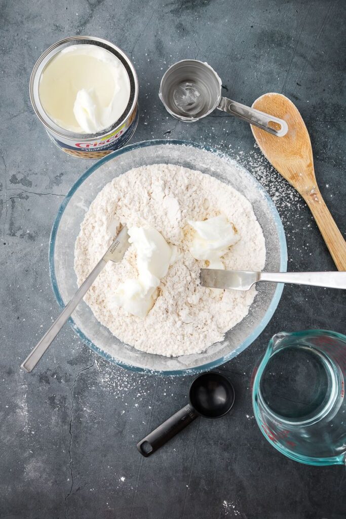 Glass bowl with two knives and flour and shortening on dark surface.