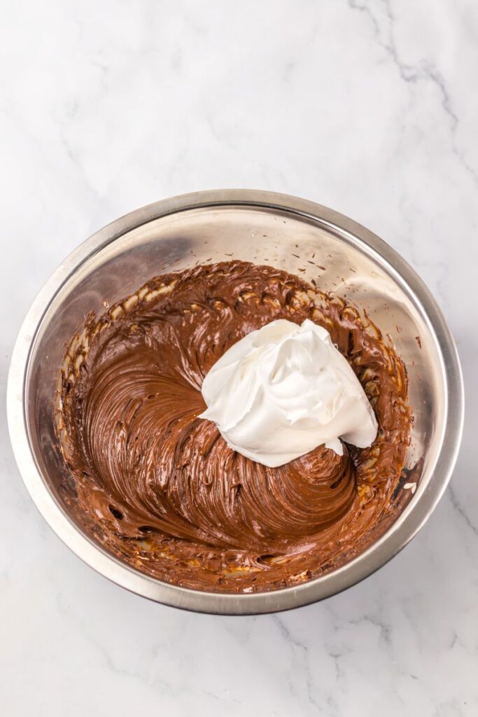 White creamy substance on top of melted chocolate in silver bowl.