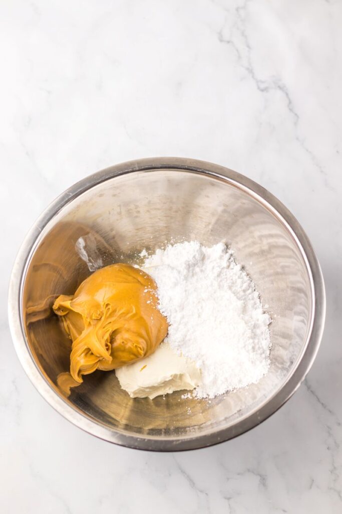 Peanut butter, powdered sugar, and cream cheese in silver bowl.