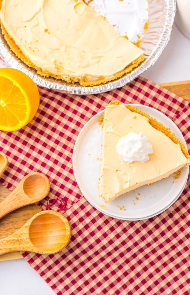Overhead view of one slice of orange pie topped with whipped cream on white plate.