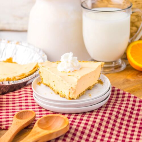 One slice of orange pie topped with whipped cream on white plate.
