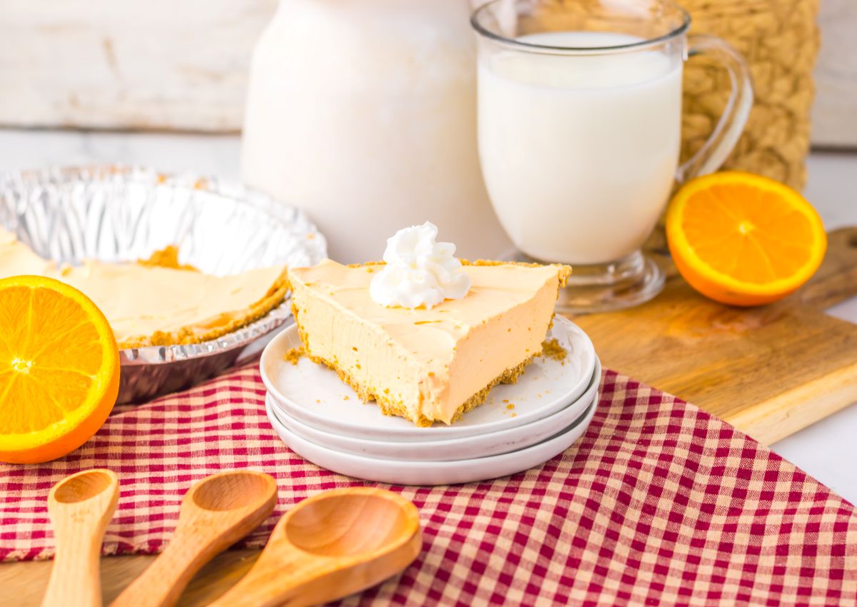 One slice of orange pie topped with whipped cream on white plate.