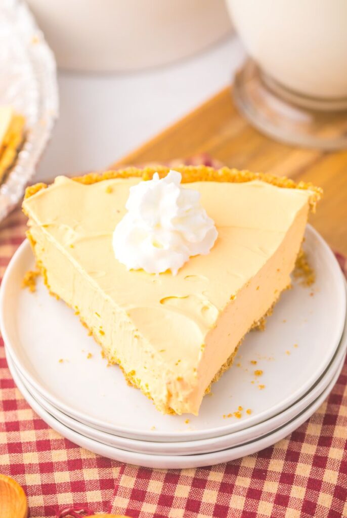 One slice of orange pie topped with whipped cream on white plate.