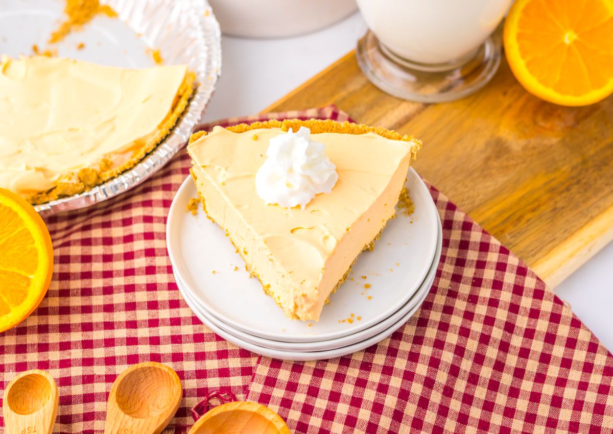 One slice of orange pie topped with whipped cream on white plate.