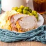 Side view of sliced pork loin on white plate with mashed potatoes and Brussels sprouts.