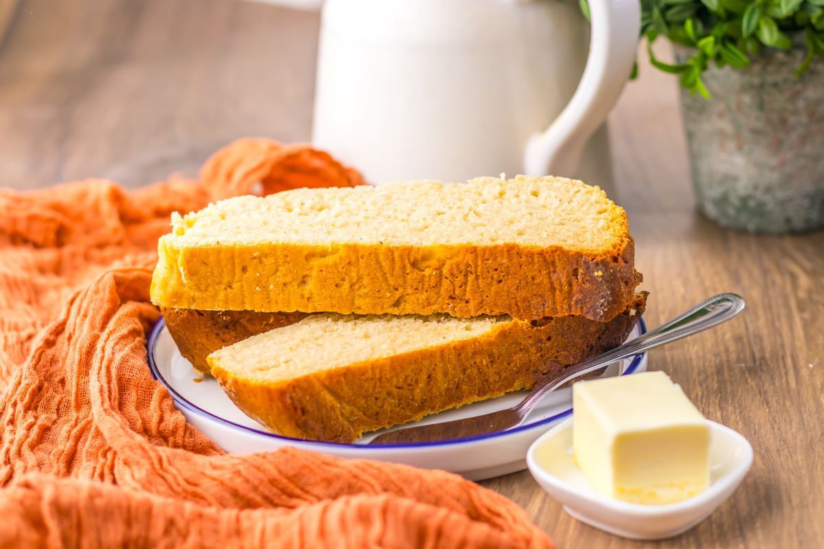 Side view of three slices of bread on white plate behind a block of butter.