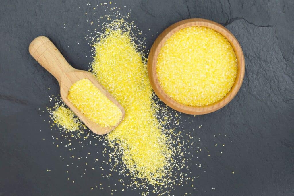 Overhead view of cornmeal in a wooden bowl next to a wooden scoop.