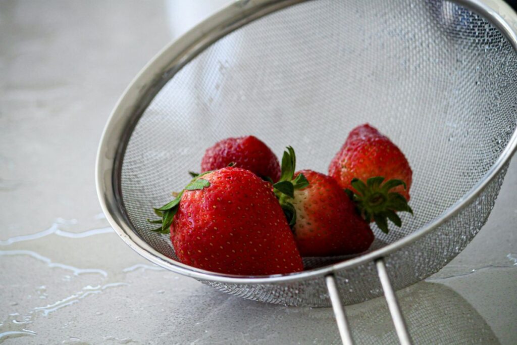 Four strawberries in metal strainer.